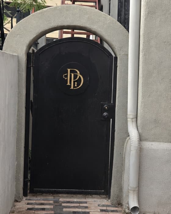 The Pour Decisions gate: an arched black iron door with a gold PD monogram and a keyhole.