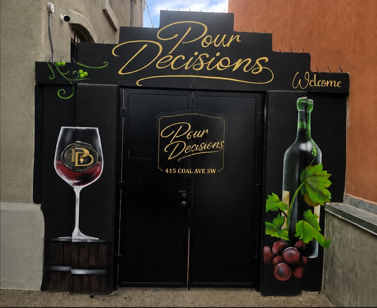 The Pour Decisions entrance at 415 Coal Ave SW: black double doors under a gold script sign, painted with a glass of red wine and a bottle with grapes.