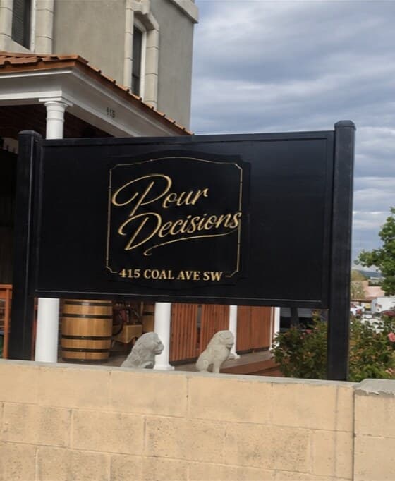 The Pour Decisions street sign at 415 Coal Ave SW: gold script on a black board in front of the club's porch.